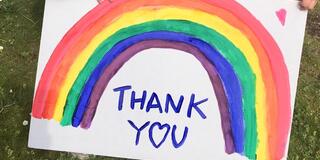A sign reading "thank you" with a rainbow above the words.