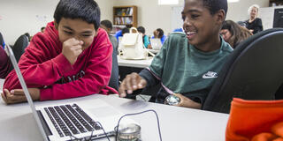 Two students sit at a desk with a computer.