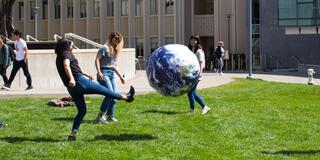 Three students playing with a big ball on Gleeson lawn
