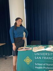 Kelsey Green in front of a table that says "University of San Francisco, School of Nursing and Health Professions"