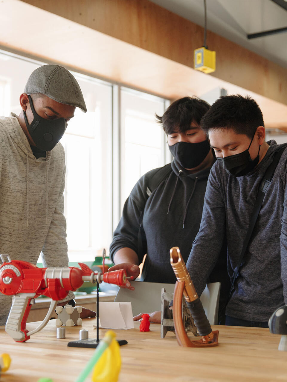 Three students look at a table with engineering experiments on it.