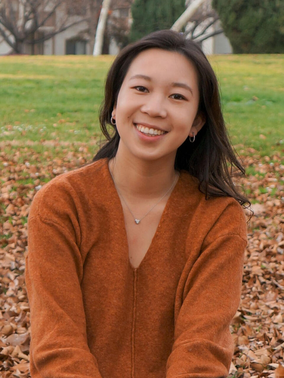 Student sits on a pile of leaves and smiles.