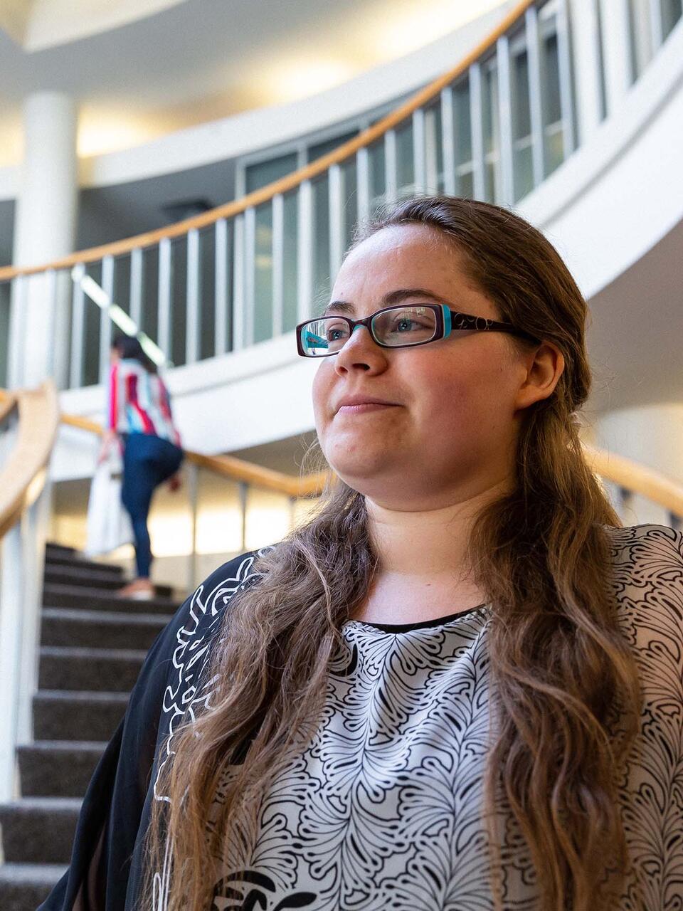 Student stands in the atrium lobby with stairs behind.