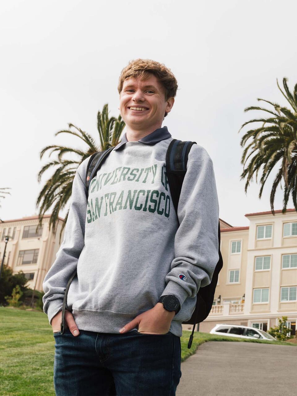 Student in USF sweatshirt stands in front of the Lone Mountain dorms.