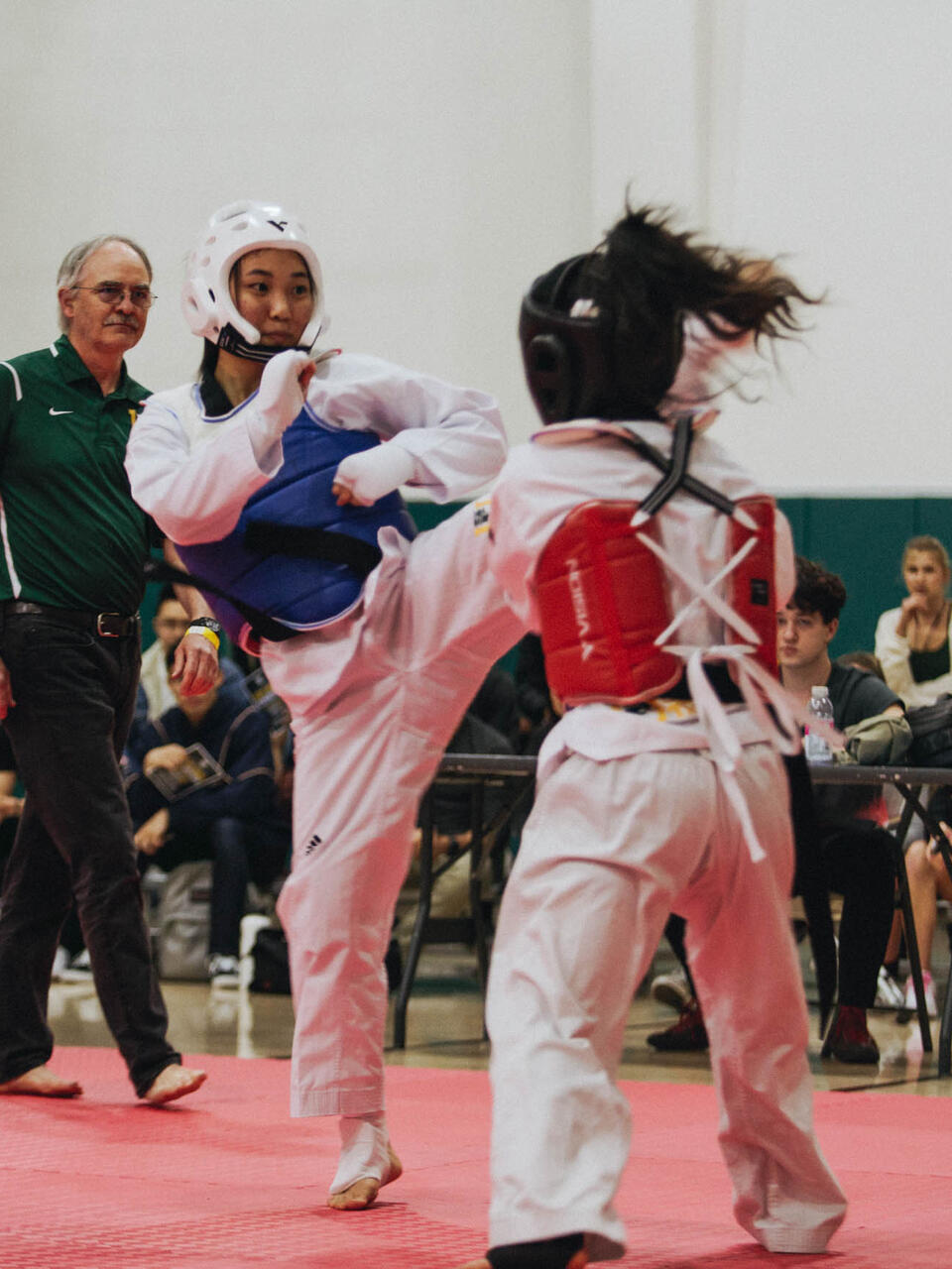 2 Taekwondo fighters with head gear sparring on the mat