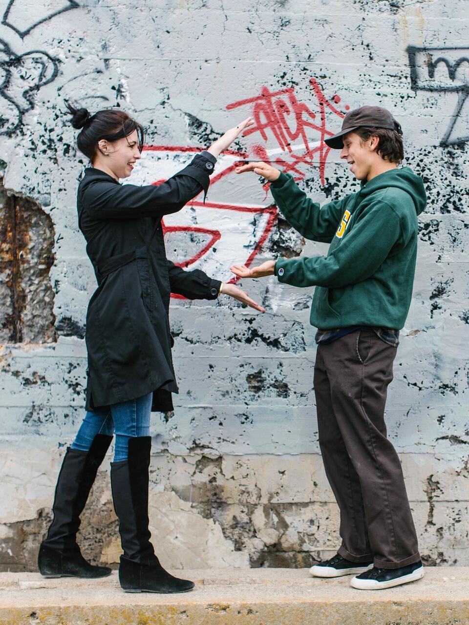 Two students stand in front of graffitied stucco wall