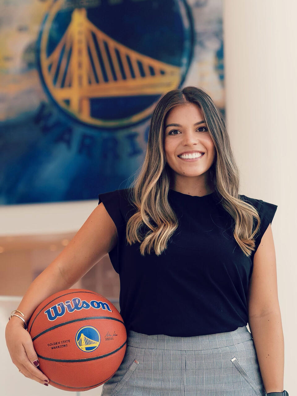 Tammy Serrato holding a basketball in front of a banner for the Warriors.