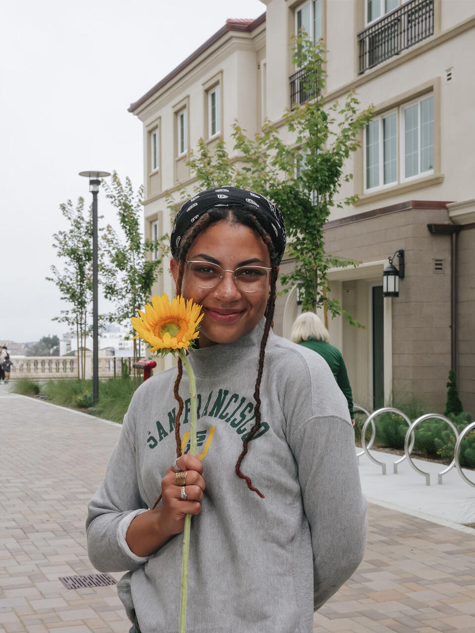 USF student holding a sunflower while standing next to Loyal Mountain residence hall